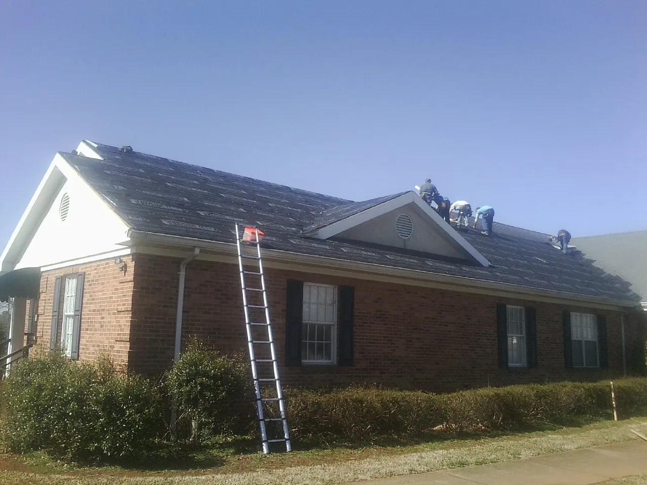 Crew tearing shingles off a brick ranch roof with a ladder set — Emergency Roof Repair work by our crew in Munster