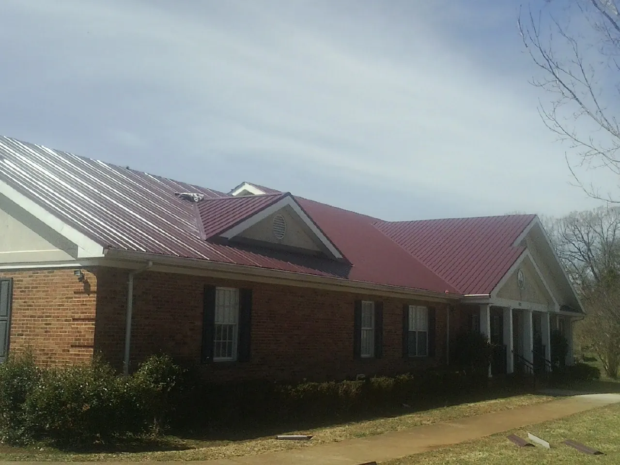 Red metal roof with gabled entries on a long brick building, from a Hail Damage Roof Repair job in Munster