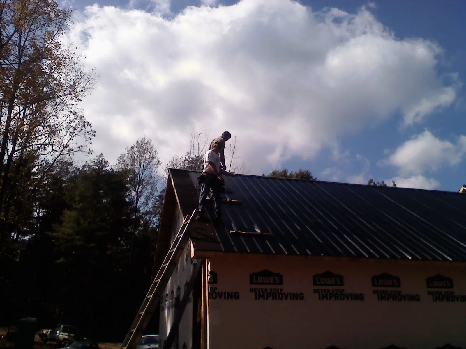 Roofer fastening dark metal panels high against a cloudy sky, from a Roof Inspection job in Munster