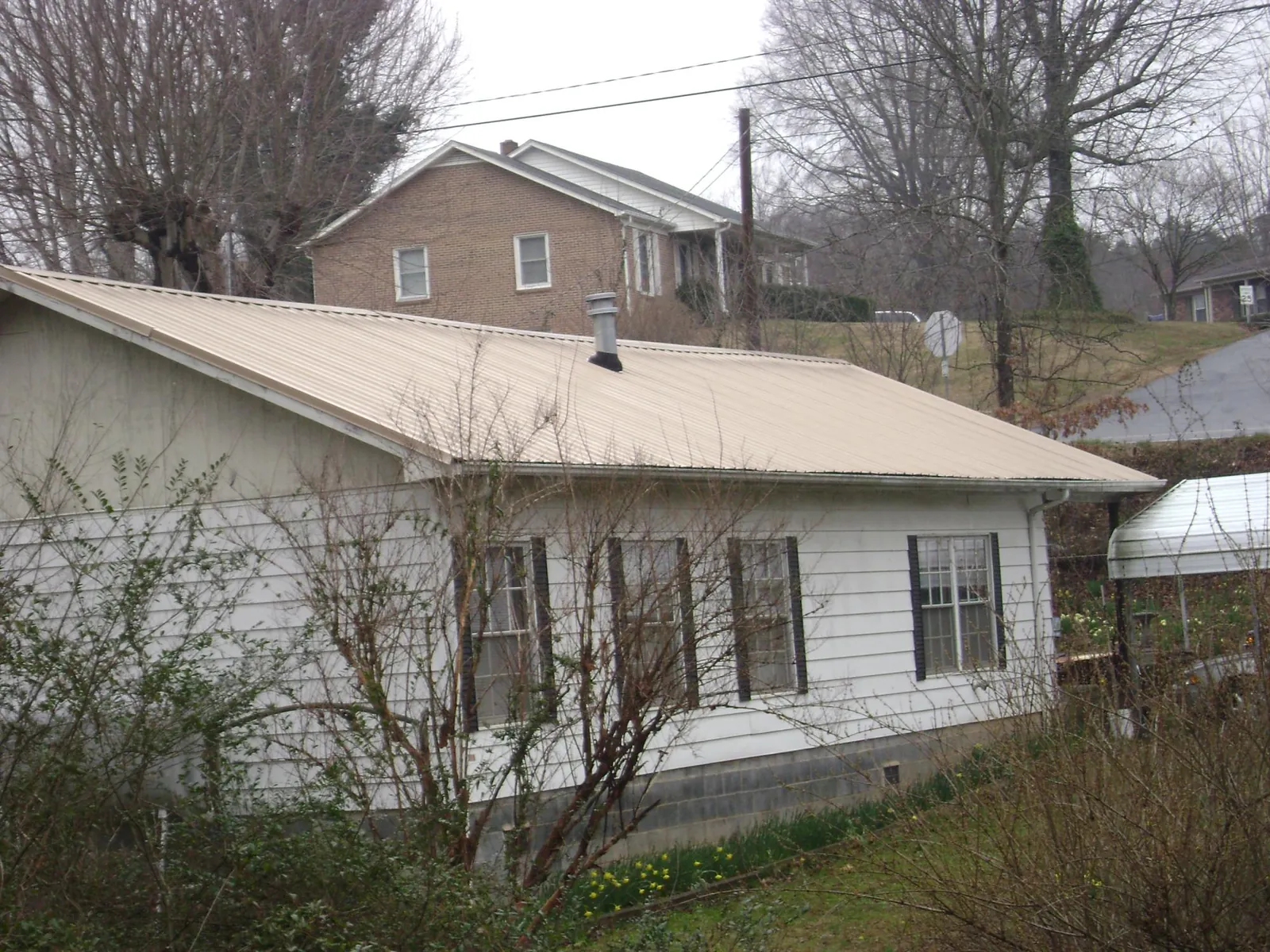 Tan metal roof on a white sided house set into a hillside — Commercial Roofing by Roofing Brothers in Munster